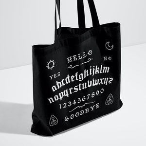 May include: Black tote bag with a white ouija board design. The design includes the letters of the alphabet, numbers 1-9 and 0, and the words "YES", "HELLO", "NO", and "GOODBYE".