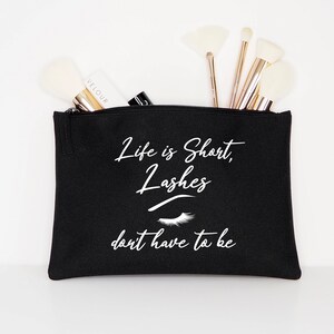 Könnte beinhalten: Schwarze Kosmetiktasche aus Canvas mit einem weißen Reißverschluss und dem Text "Life is short, lashes don't have to be" mit einer weißen Wimperngrafik.