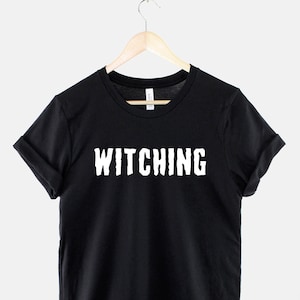 May include: Black t-shirt with white text that reads "Witching" on a black hanger.