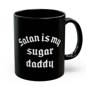 Puede incluir: Taza de caf&eacute; de cer&aacute;mica negra con texto blanco que dice "Satan is my sugar daddy".