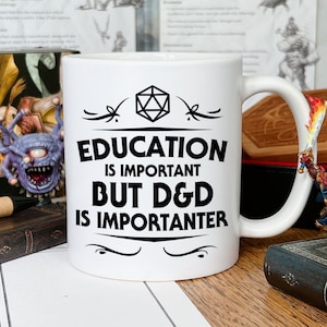 以下が含まれることがあります： 白いセラミック製のマグカップに、黒いデザインで「教育は重要だが、D&Dはもっと重要だ」と書かれている。テキストの上に、黒と白のサイコロのアイコンがある。マグカップは木製のテーブルの上に置かれている