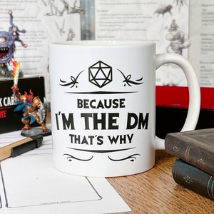 May include: White ceramic mug with a black design featuring a 20-sided die and the text "Because I'm the DM That's Why".