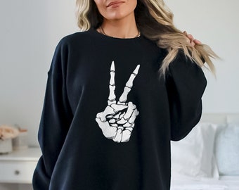 May include: Black sweatshirt featuring a white skeleton hand making a peace sign. The graphic is centered on the front of the long-sleeved top. The sweatshirt is a casual style, suitable for everyday wear.