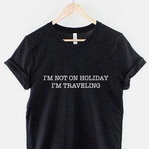May include: Black t-shirt with white text that reads "I'm not on holiday I'm traveling".