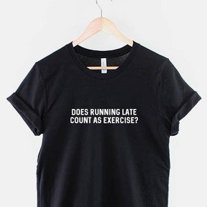 Könnte beinhalten: Schwarzes T-Shirt mit dem weißen Text "DOES RUNNING LATE COUNT AS EXERCISE?". Das T-Shirt hängt an einem Holzbügel, der an einer Metallkette befestigt ist. Die Ärmel sind umgeschlagen.