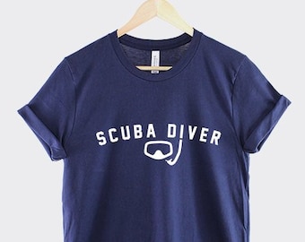 May include: A navy blue t-shirt with white text that reads "SCUBA DIVER" and a white scuba mask and snorkel graphic.
