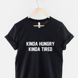 K&ouml;nnte beinhalten: Schwarzes T-Shirt mit wei&szlig;em Text, der "Kinda Hungry Kinda Tired" lautet.