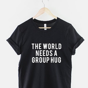 May include: Black t-shirt with white text that reads "The World Needs A Group Hug."