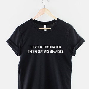Puede incluir: Camiseta negra con texto blanco que dice "They're not swearwords They're sentence enhancers".