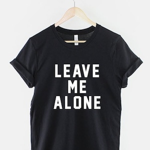 Op de afbeelding: Zwart T-shirt met witte tekst die "LEAVE ME ALONE" zegt.