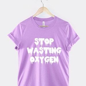 May include: A purple t-shirt with the text "STOP WASTING OXYGEN" in white dripping letters.