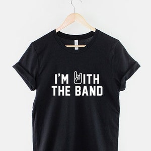 Puede incluir: Camiseta negra con texto blanco que dice "I'm with the band" y un gesto de mano de rock and roll.
