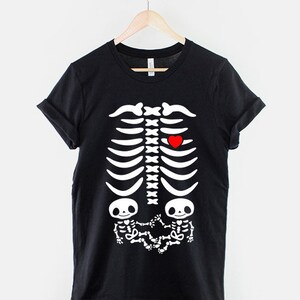 May include: Black t-shirt with a white skeleton graphic. The skeleton has a red heart in the chest area and two smaller skeletons in the stomach area.