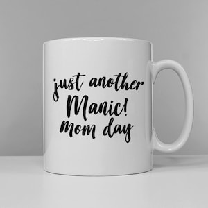 May include: White ceramic coffee mug with black text that reads "just another manic! mom day"