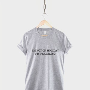 May include: Gray t-shirt with the text "I'm not on holiday I'm traveling" printed in black.