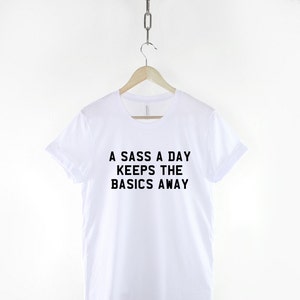 May include: White t-shirt with black text that reads "A sass a day keeps the basics away."