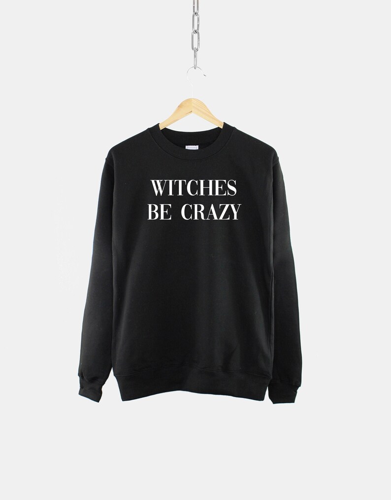 Op de afbeelding: Zwart sweatshirt met witte tekst die "WITCHES BE CRAZY" zegt.