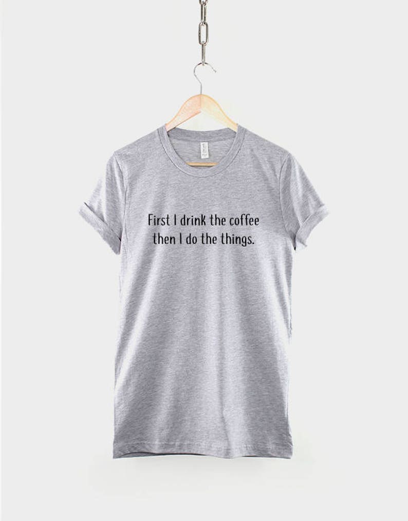 May include: Gray t-shirt with the text "First I drink the coffee then I do the things."