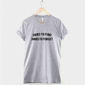 May include: A heather grey t-shirt with the text "HARD TO FIND HARD TO FORGET" printed in black.