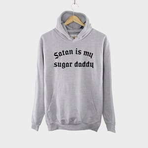K&ouml;nnte beinhalten: Grauer Kapuzenpullover mit dem Aufdruck "Satan is my sugar daddy" in schwarzer gotischer Schrift.