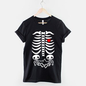 May include: Black t-shirt with a white skeleton graphic. The skeleton has a red heart in the chest area and two smaller skeletons in the stomach area.