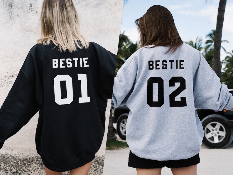 Puede incluir: Dos sudaderas grises con la palabra "BESTIE" y los n&uacute;meros "01" y "02" impresos en la espalda. Las sudaderas las llevan dos personas de espaldas.