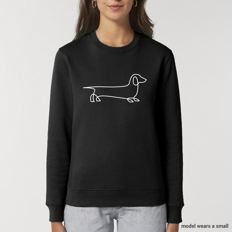 Może przedstawiać: Czarny sweter z białym rysunkiem linii psa rasy dachshund.