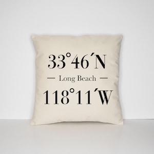 Könnte beinhalten: Ein weißes Kissen mit schwarzem Text, der "33°46'N - Long Beach - 118°11'W" lautet.