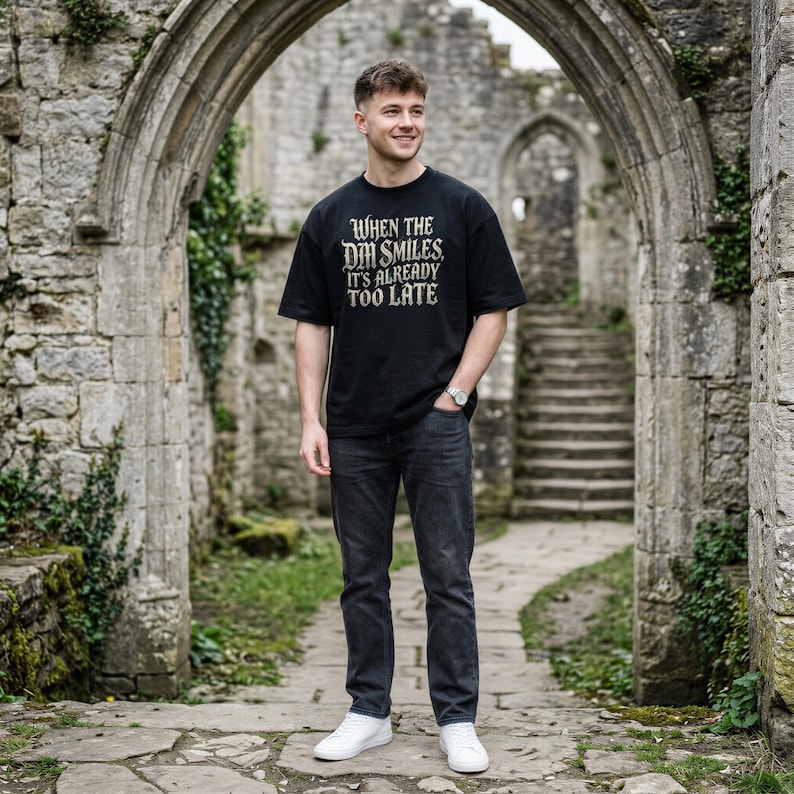 May include: A black short-sleeved t-shirt featuring the white text "WHEN THE DM SMILES, IT'S ALREADY TOO LATE" printed on the chest, paired with dark gray denim jeans and white sneakers.