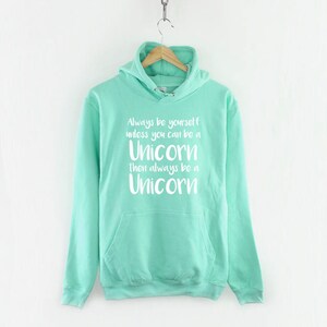 May include: A turquoise blue hooded sweatshirt with a white graphic print that reads "Always be yourself unless you can be a Unicorn then always be a Unicorn".