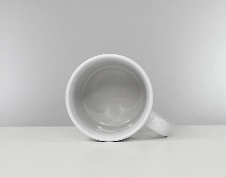 May include: A white ceramic mug with a rounded handle. The mug is empty and has a smooth, glossy finish.