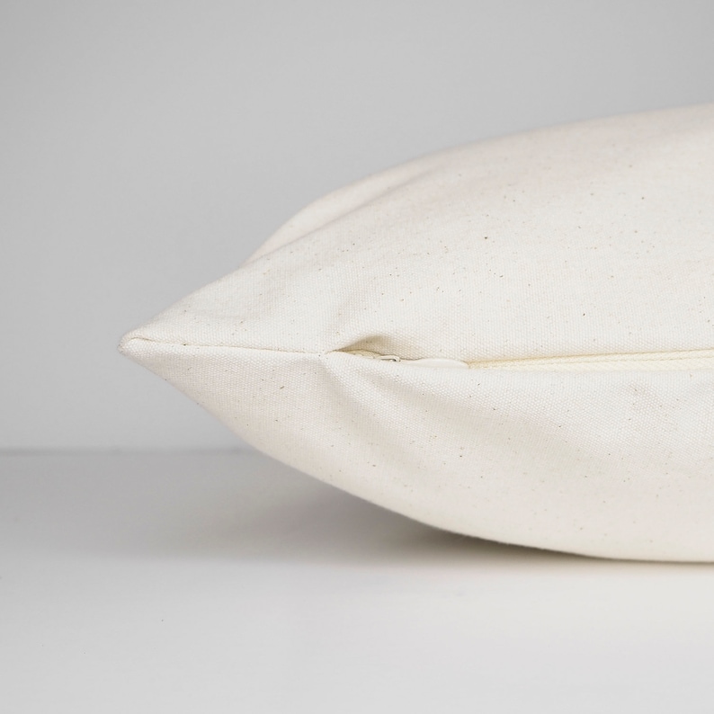 May include: Close-up of a white pillow cover with a zipper closure. The fabric has a subtle texture.