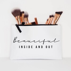 May include: White zippered makeup bag with the text "Beautiful Inside and Out" in black lettering. The bag is filled with makeup brushes.