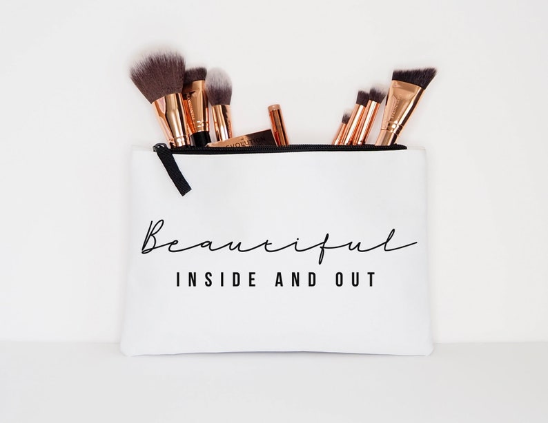 May include: White zippered makeup bag with the text "Beautiful Inside and Out" in black lettering. The bag is filled with makeup brushes.
