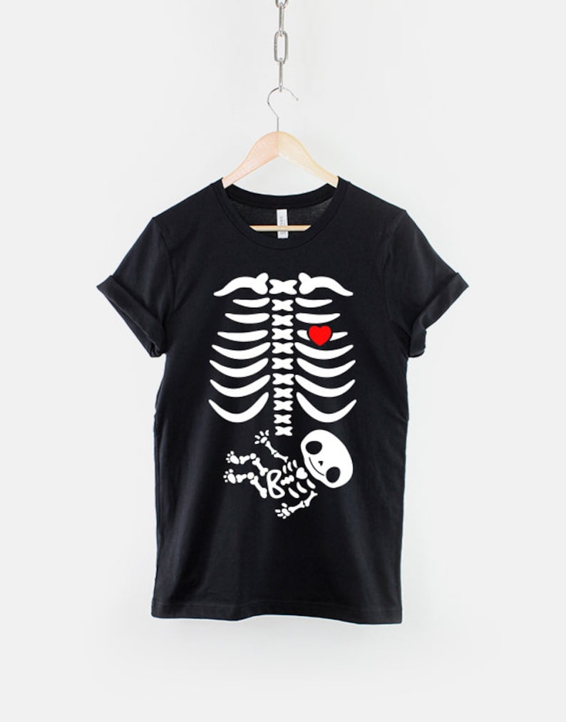 May include: Black t-shirt with a white skeleton graphic. The skeleton has a red heart in its chest and a smaller white skeleton baby in its belly.