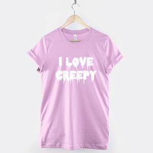 Puede incluir: Una camiseta rosa claro con el texto "I LOVE CREEPY" en letras blancas que gotean.
