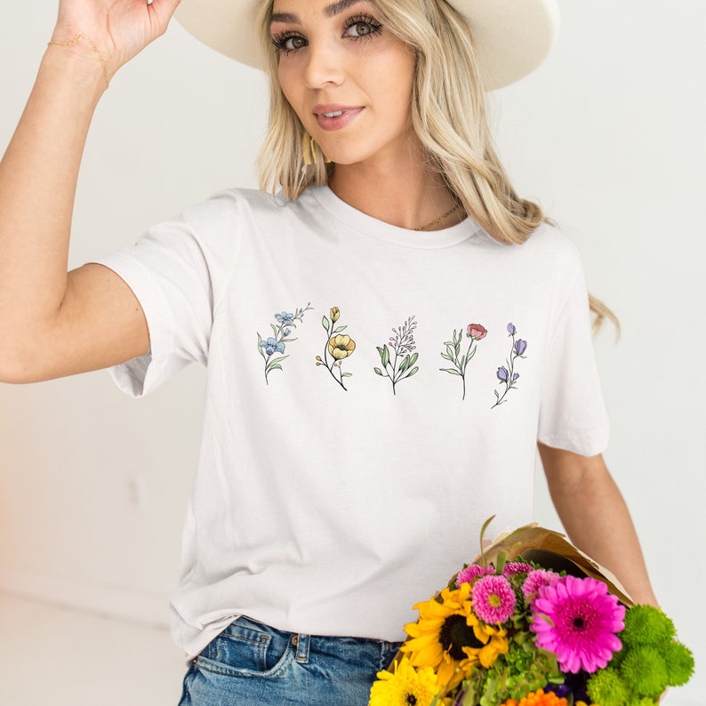 May include: White t-shirt with a floral design featuring five different flowers in shades of blue, yellow, pink, red, and purple.