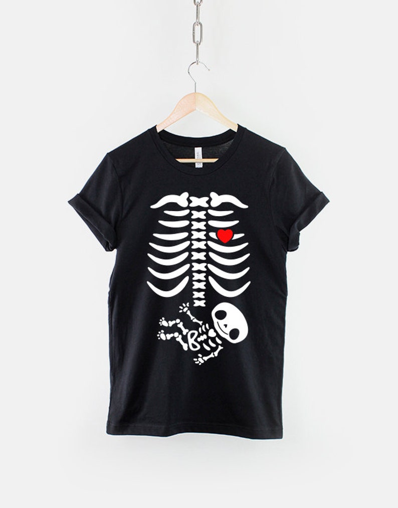 May include: Black t-shirt with a white skeleton graphic. The skeleton has a red heart in its chest and a smaller white skeleton baby in its belly.