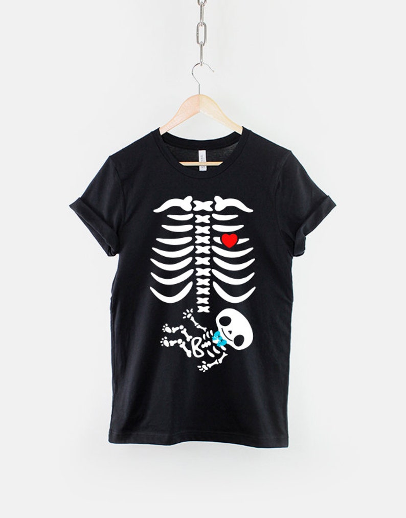May include: Black t-shirt with a white skeleton graphic. The skeleton has a red heart and a small baby skeleton with a blue bow tie inside its ribcage.