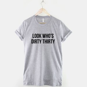 Może przedstawiać: Szary T-shirt z nadrukiem "LOOK WHO'S DIRTY THIRTY" w kolorze czarnym.