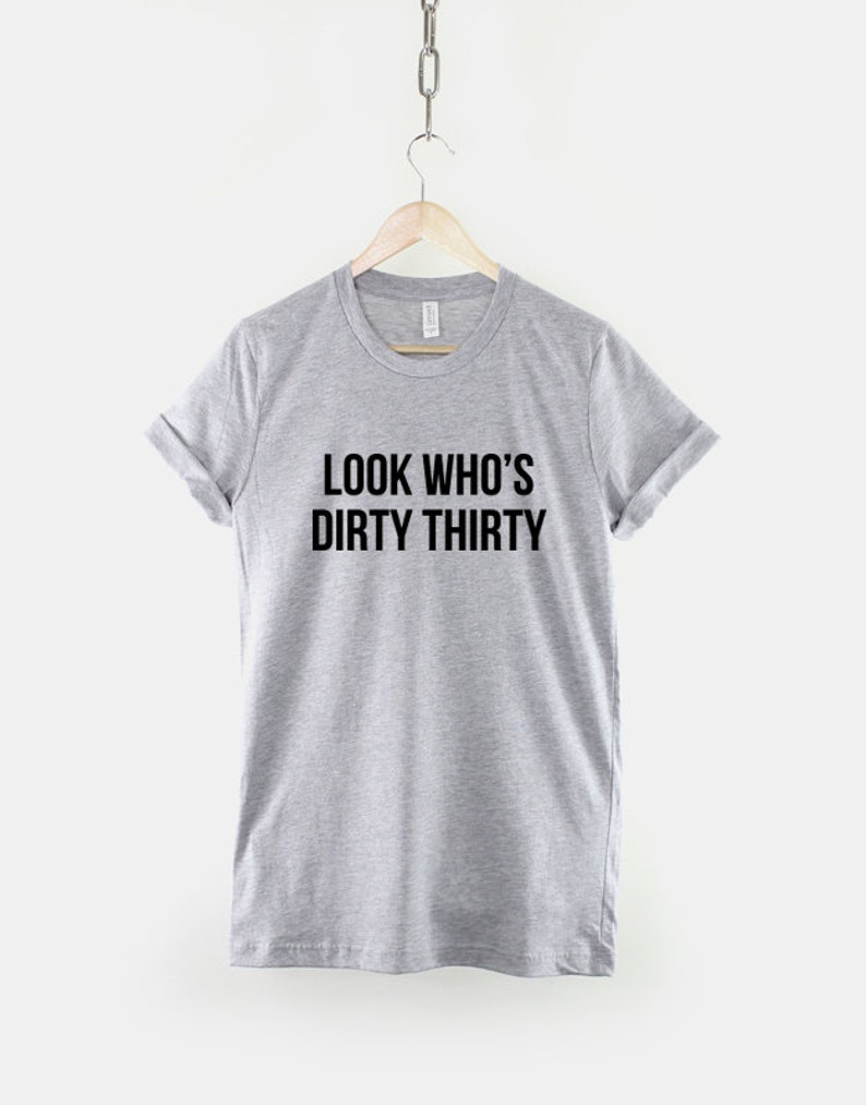 Może przedstawiać: Szary T-shirt z nadrukiem "LOOK WHO'S DIRTY THIRTY" w kolorze czarnym.