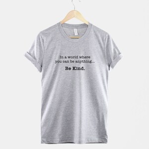 May include: A heather grey t-shirt with the text "In a world where you can be anything... Be Kind."