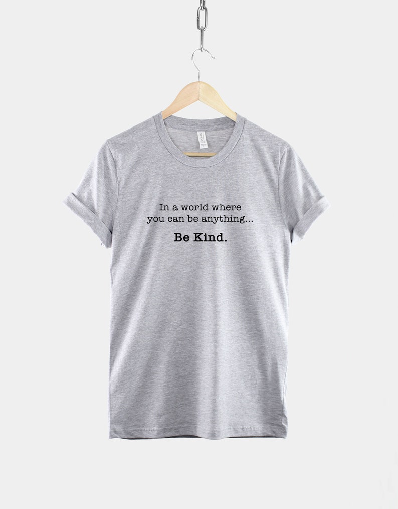 May include: A heather grey t-shirt with the text "In a world where you can be anything... Be Kind."
