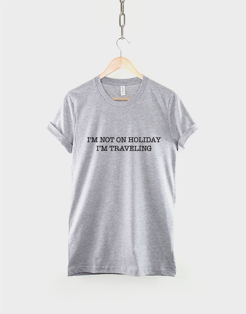 May include: Gray t-shirt with the text "I'm not on holiday I'm traveling" printed in black.
