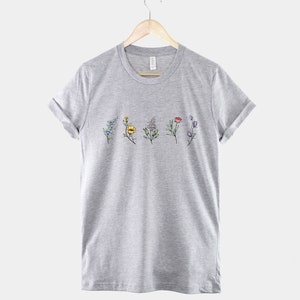 May include: A heather grey t-shirt with a row of colourful flowers printed on the front.
