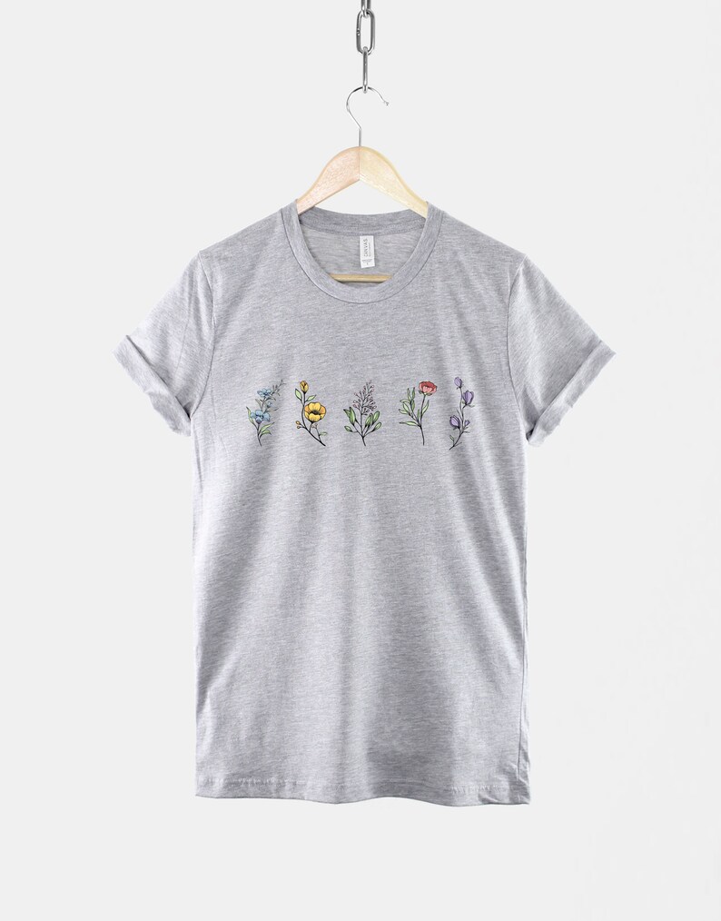 May include: A heather grey t-shirt with a row of colourful flowers printed on the front.