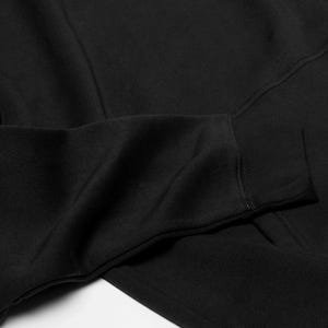 May include: A solid black long-sleeve sweatshirt featuring a ribbed cuff at the end of the sleeve. The fabric has a smooth, consistent texture throughout, with visible seams along the arm and cuff area, showcasing a simple and functional design.