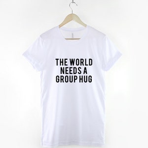 May include: White t-shirt with black text that reads "The World Needs a Group Hug."