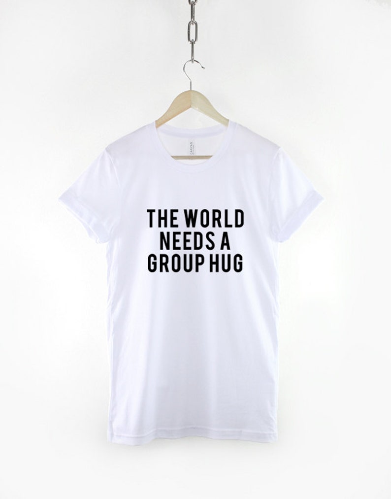 May include: White t-shirt with black text that reads "The World Needs a Group Hug."