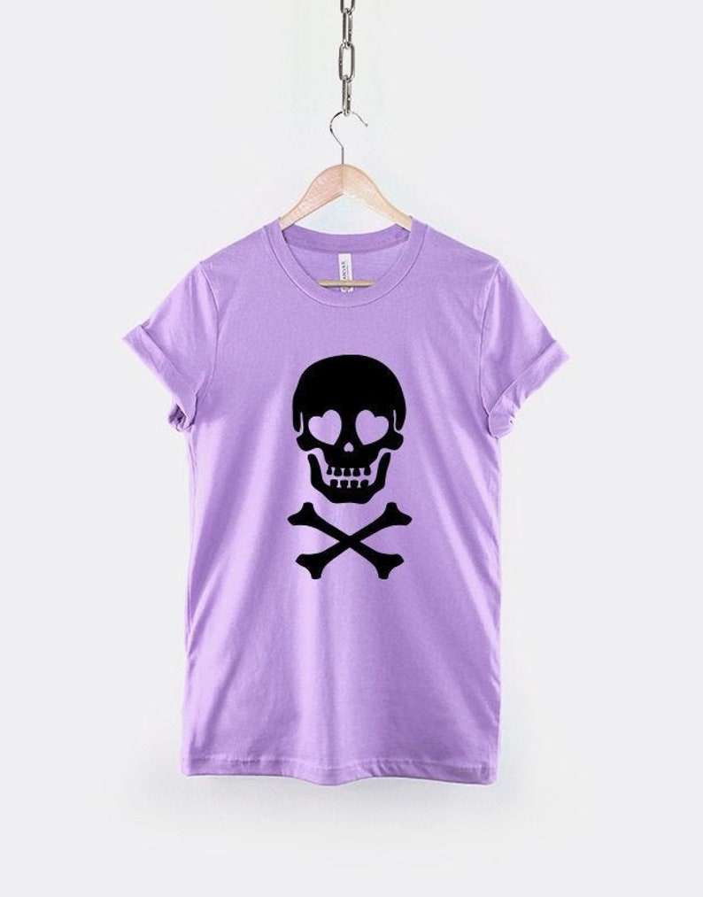 May include: A lavender t-shirt with a black skull and crossbones design. The skull has heart-shaped eyes.